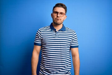 Young man with blue eyes wearing glasses and casual striped t-shirt over blue background depressed and worry for distress, crying angry and afraid. Sad expression.