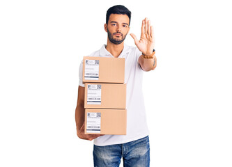 Young handsome hispanic man holding delivery package with open hand doing stop sign with serious and confident expression, defense gesture