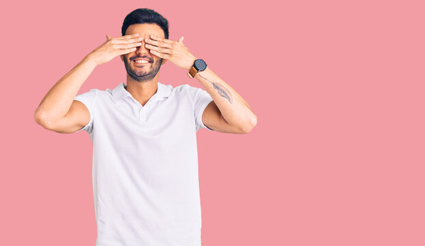 Young handsome hispanic man wearing casual clothes covering eyes with hands smiling cheerful and funny. blind concept.