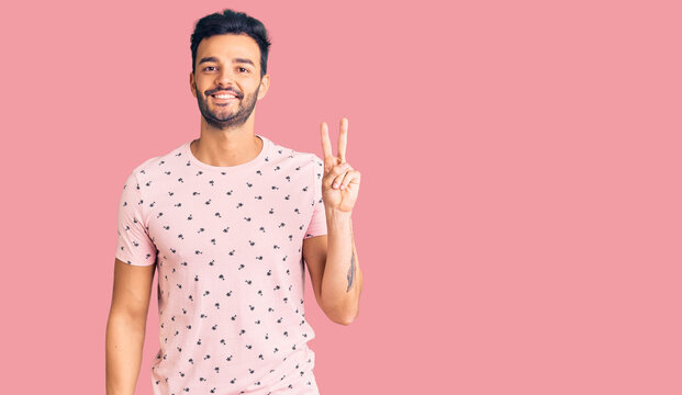 Young handsome hispanic man wearing casual clothes smiling with happy face winking at the camera doing victory sign. number two.