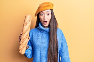 Young beautiful blonde woman wearing french beret holding bread scared and amazed with open mouth for surprise, disbelief face