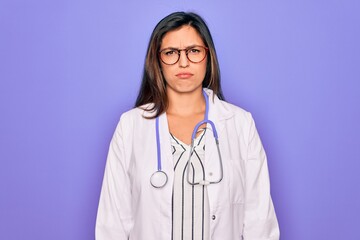Professional doctor woman wearing stethoscope and medical coat over purple background depressed and worry for distress, crying angry and afraid. Sad expression.