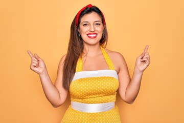 Young hispanic pin up woman wearing fashion sexy 50s style over yellow background smiling confident pointing with fingers to different directions. Copy space for advertisement