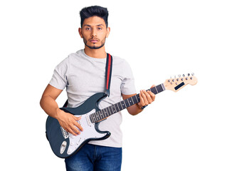 Handsome latin american young man playing electric guitar thinking attitude and sober expression looking self confident