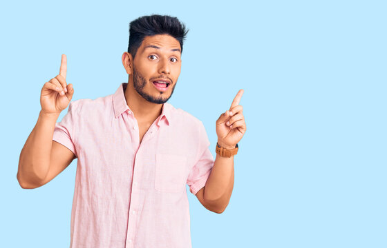 Handsome latin american young man wearing casual summer shirt smiling amazed and surprised and pointing up with fingers and raised arms.