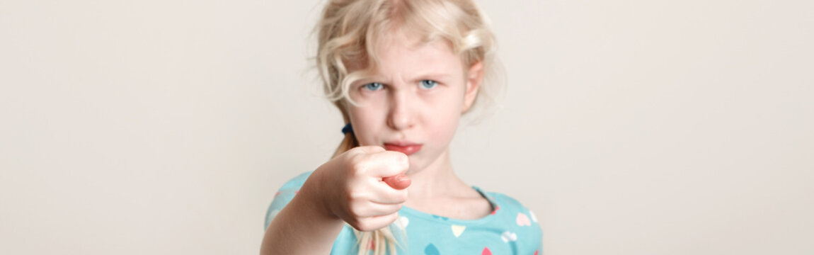 Child girl showing fig sign. Kid expressing strong negative emotion. Cute adorable blonde Caucasian preschool girl posing in studio on light background. Web banner header for a website.