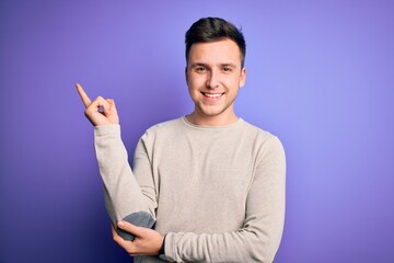 Young handsome caucasian man wearing casual sweater over purple isolated background with a big smile on face, pointing with hand and finger to the side looking at the camera.