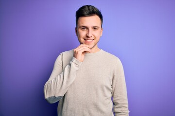 Young handsome caucasian man wearing casual sweater over purple isolated background looking confident at the camera with smile with crossed arms and hand raised on chin. Thinking positive.