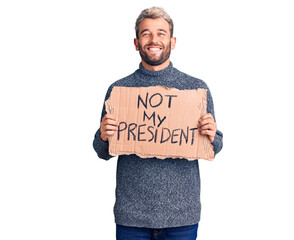 Young handsome blond man holding not my president cardboard banner looking positive and happy standing and smiling with a confident smile showing teeth