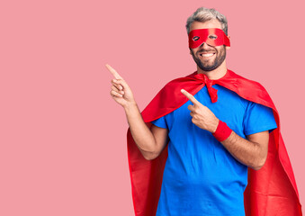 Young blond man wearing super hero custome smiling and looking at the camera pointing with two hands and fingers to the side. © Krakenimages.com