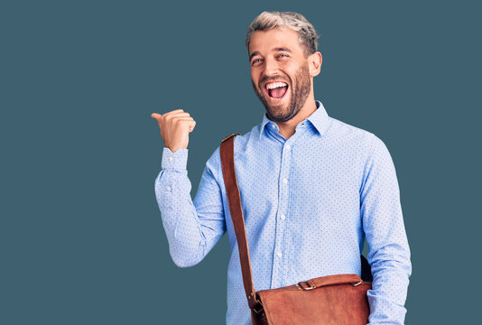 Young handsome blond man wearing elegant shirt holding briefcase pointing thumb up to the side smiling happy with open mouth