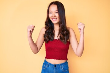 Young beautiful chinese girl wearing summer clothes screaming proud, celebrating victory and success very excited with raised arms