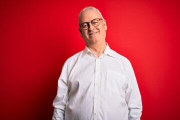 Middle age handsome hoary man wearing casual shirt and glasses over red background with a happy and cool smile on face. Lucky person.