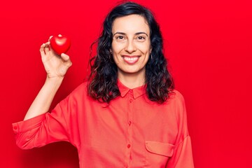 Young beautiful hispanic woman holding heart looking positive and happy standing and smiling with a...