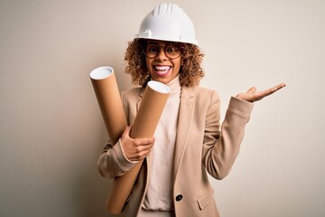 African american curly architect woman wearing safety helmet and glasses holding blueprints very happy and excited, winner expression celebrating victory screaming with big smile and raised hands