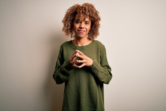 Beautiful african american woman with curly hair wearing casual sweater over white background Hands together and fingers crossed smiling relaxed and cheerful. Success and optimistic
