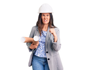 Young beautiful brunette woman wearing architect hardhat holding blueprint annoyed and frustrated...