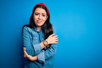 Young brunette woman wearing casual denim shirt over blue isolated background shaking and freezing for winter cold with sad and shock expression on face
