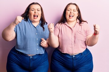 Young plus size twins wearing casual clothes angry and mad raising fists frustrated and furious while shouting with anger. rage and aggressive concept.