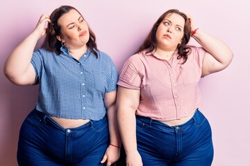 Young plus size twins wearing casual clothes confuse and wondering about question. uncertain with doubt, thinking with hand on head. pensive concept.