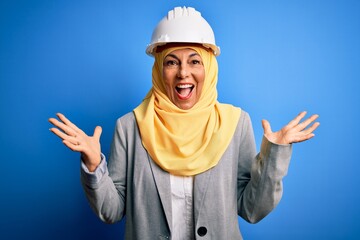 Middle age brunette architect woman wearing muslim traditional hijab and security helmet celebrating crazy and amazed for success with arms raised and open eyes screaming excited. Winner concept