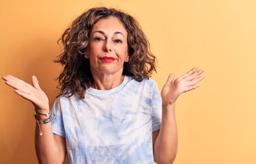 Middle age beautiful woman wearing casual dye t-shirt standing over yellow background clueless and...