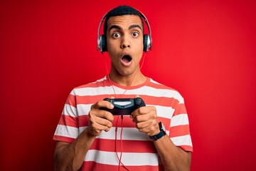 Handsome african american gamer man playing video game using jostick and headphones scared in shock...
