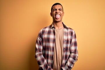 Young handsome african american man wearing casual shirt standing over yellow background sticking tongue out happy with funny expression. Emotion concept.