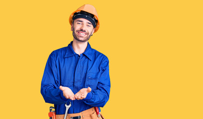 Young hispanic man wearing worker uniform smiling with hands palms together receiving or giving gesture. hold and protection