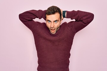 Young handsome man with blue eyes wearing casual sweater standing over pink background Crazy and scared with hands on head, afraid and surprised of shock with open mouth