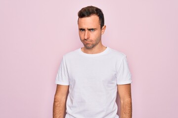 Handsome man with blue eyes wearing casual white t-shirt standing over pink background skeptic and nervous, frowning upset because of problem. Negative person.