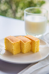 Close up stack of butter cake in a white plate on white table with a cup of milk blurred background.