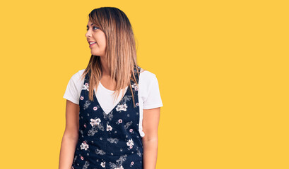 Young beautiful woman wearing casual floral dress looking away to side with smile on face, natural expression. laughing confident.