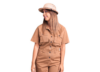 Young beautiful woman wearing explorer hat looking away to side with smile on face, natural expression. laughing confident.