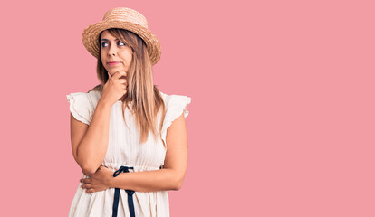 Young beautiful woman wearing summer hat and t-shirt with hand on chin thinking about question, pensive expression. smiling with thoughtful face. doubt concept.