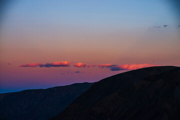 Atmospheric minimal dawn landscape with dark silhouette of mountains under vivid lilac blue gradient sky with pink clouds on sunset. Beautiful mountain scenery with mountain silhouettes on sunrise.