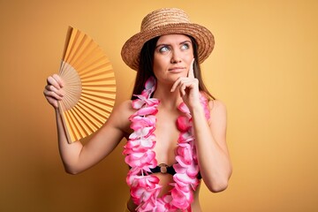 Young beautiful woman with blue eyes on vacation wearing bikini holding hand fan serious face thinking about question, very confused idea