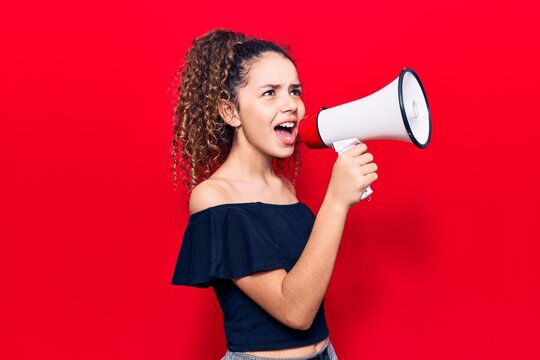 Adorable latin teenager girl with angry expression. Screaming loud using megaphone standing over isolated red background