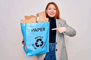 Young beautiful redhead woman recycling holding paper bag with cardboard to recycle very happy pointing with hand and finger