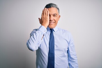 Middle age handsome grey-haired business man wearing elegant shirt and tie covering one eye with hand, confident smile on face and surprise emotion.