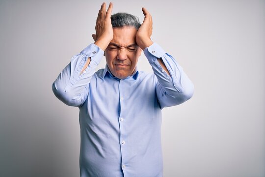 Middle age handsome grey-haired business man wearing elegant shirt over white background suffering from headache desperate and stressed because pain and migraine. Hands on head.