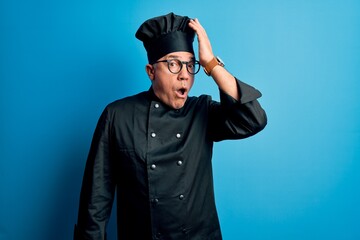 Middle age handsome grey-haired chef man wearing cooker uniform and hat surprised with hand on head for mistake, remember error. Forgot, bad memory concept.