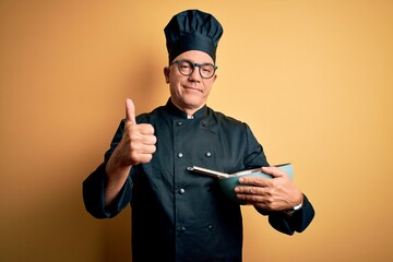 Middle age handsome grey-haired chef man wearing cooker uniform and hat using whisk happy with big smile doing ok sign, thumb up with fingers, excellent sign