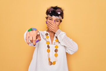 Young beautiful african american afro hippie woman wearing sunglasses and accessories laughing at you, pointing finger to the camera with hand over mouth, shame expression