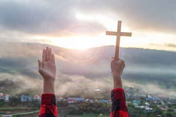 Human praying to the GOD while holding a crucifix symbol with bright sunbeam on the sky