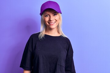 Young beautiful blonde woman wearing t-shirt and purple cap over isolated background with a happy and cool smile on face. Lucky person.