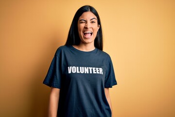 Young beautiful hispanic woman wearing volunteer t-shirt as social charity moral winking looking at...