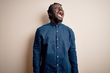 Obraz premium Young handsome african american man wearing casual shirt standing over white background angry and mad screaming frustrated and furious, shouting with anger. Rage and aggressive concept.