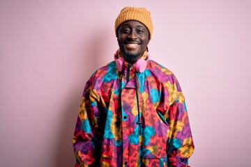 Young handsome african american man wearing colorful coat and cap over pink background with a happy and cool smile on face. Lucky person.