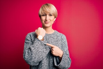 Young blonde woman with modern short hair wearing casual sweater over pink background In hurry...